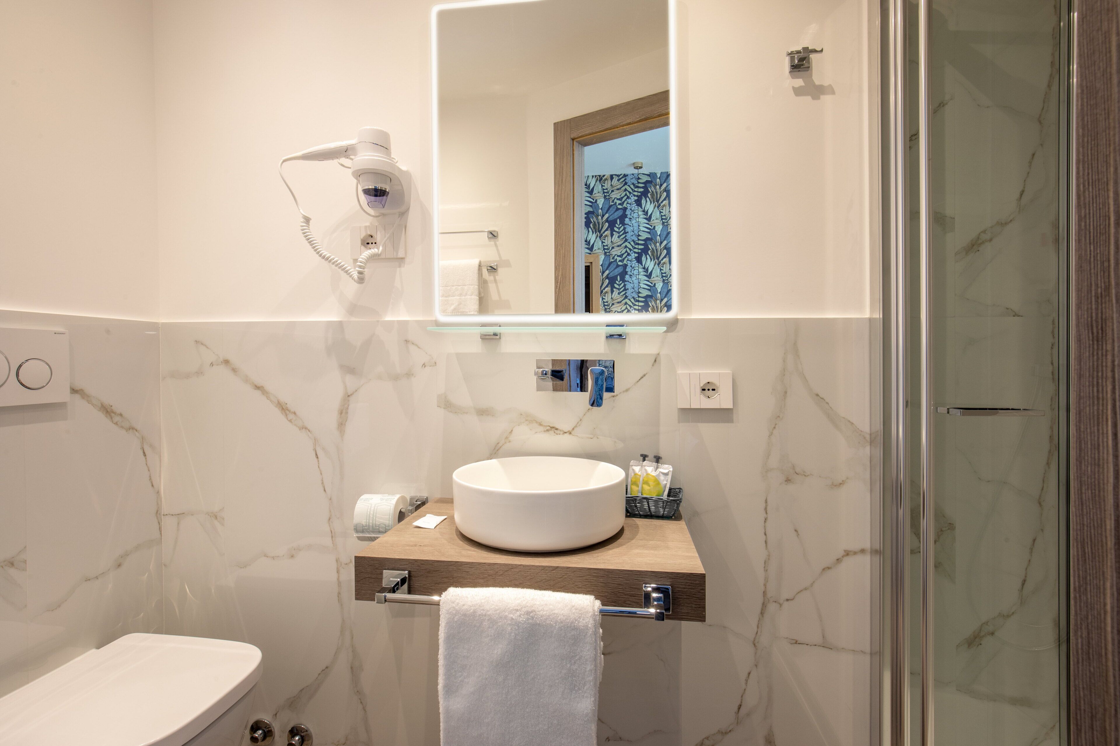 A bathroom with a marble wall, a round sink, a towel rack, a mirror, and a hairdryer.