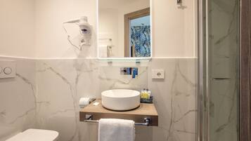 A bathroom with a marble wall, a round sink, a towel rack, a mirror, and a hairdryer.