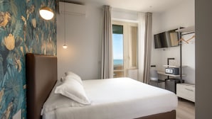 A hotel room with a bed, a desk, a chair, a TV, and a view of the sea. - Hotel La Scaletta (Rome)