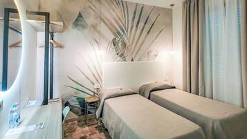 A hotel room with two single beds, a desk with a chair, a mirror, and a plant.