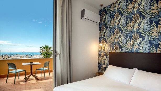 A hotel room with a bed, a small table with chairs, a view of the beach, and a patterned wall. - Hotel La Scaletta (Rome)