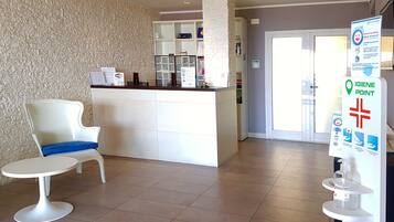 A reception area with a white reception desk, a white chair with a blue cushion, and a 'WiFi' sign. There is a 'Hotel Scalista' sign on the wall and a 'GIGIENE POINT' sign on the right.