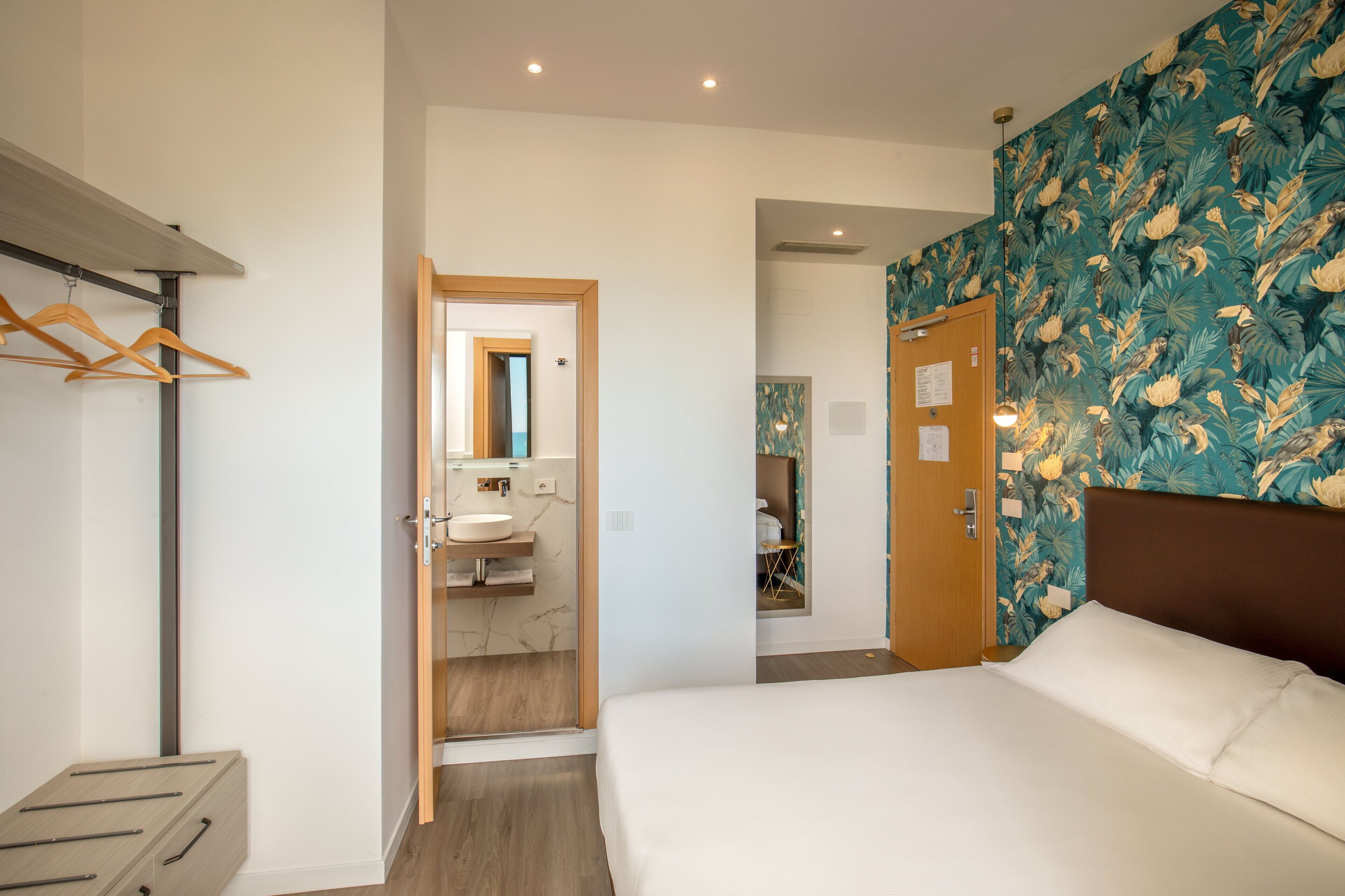 Un dormitorio con cama, armario, baño con lavamanos y una puerta que da a otra habitación.