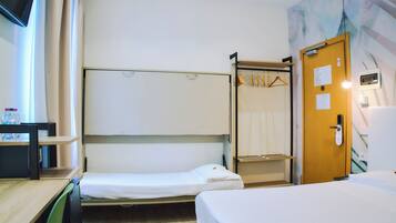 Habitación de hotel con literas, un escritorio con silla, un armario y una puerta con espejo y perchero.