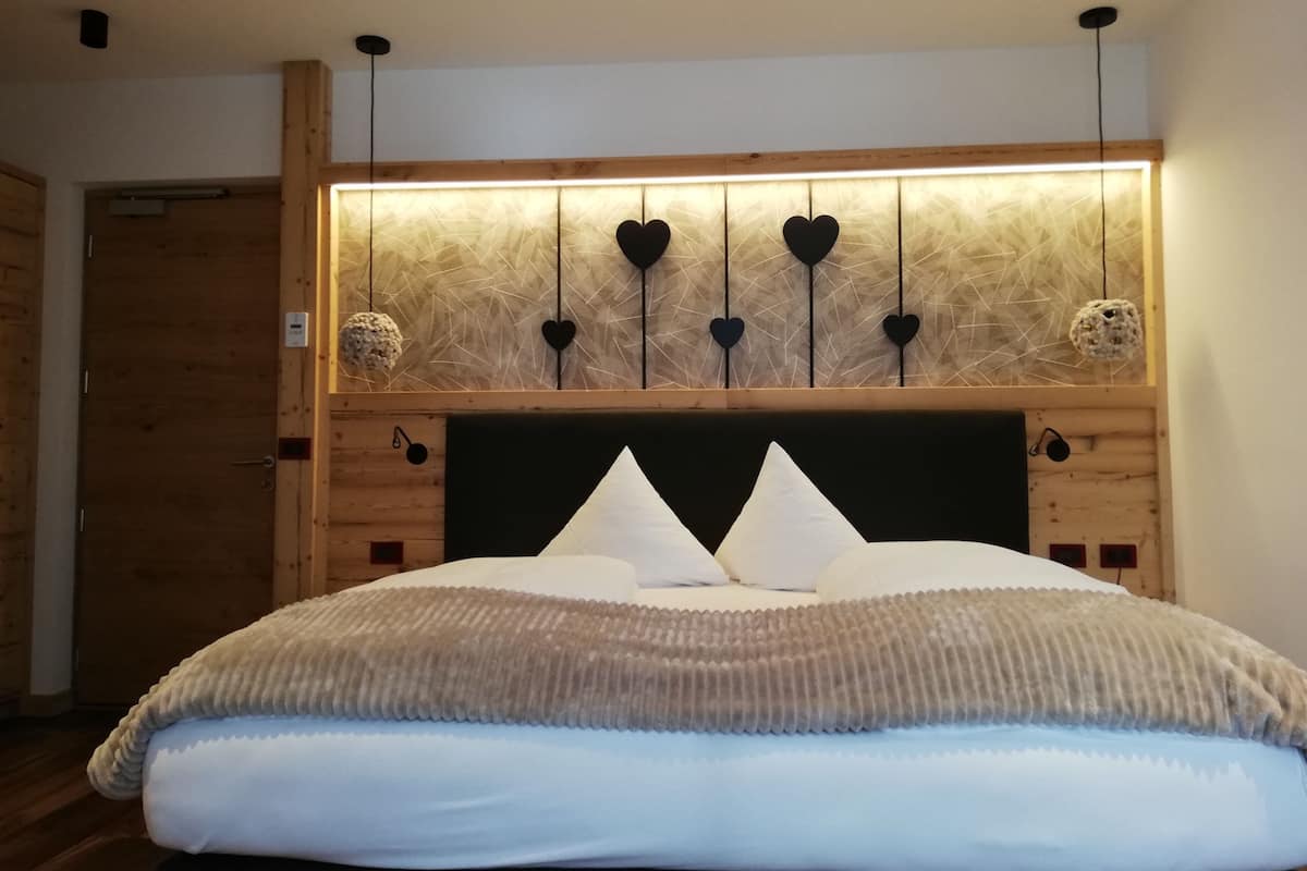 Un dormitorio con cabecera de madera, una cama grande con ropa de cama blanca y beige, y una pared con diseño geométrico y adornos con forma de corazón.