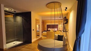 Ein modernes Schlafzimmer mit einem runden Bett, einer Duschkabine aus Glas und einem Holzboden.