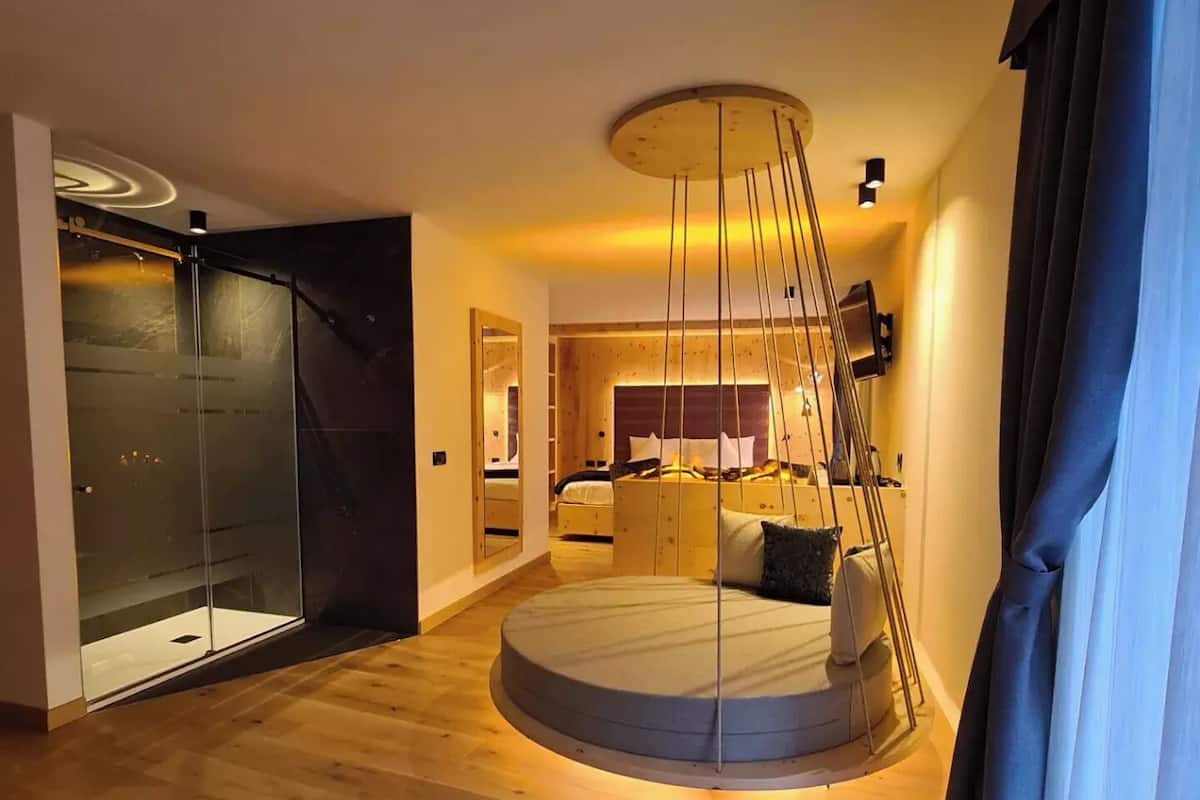 Un dormitorio moderno con una cama redonda, cabina de ducha de vidrio y piso de madera.