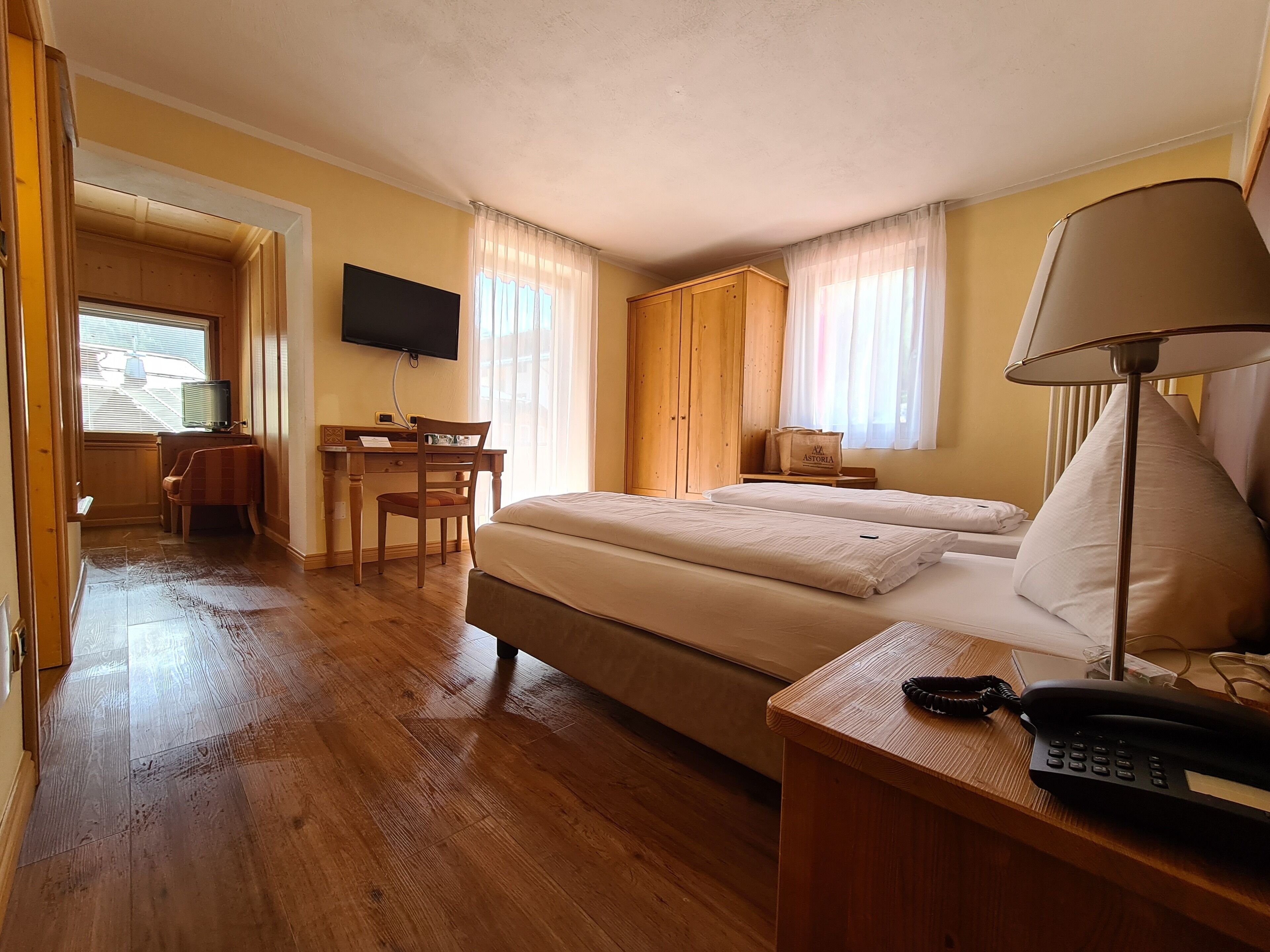 A hotel room with a bed, a desk with a chair, a television, and a lamp.