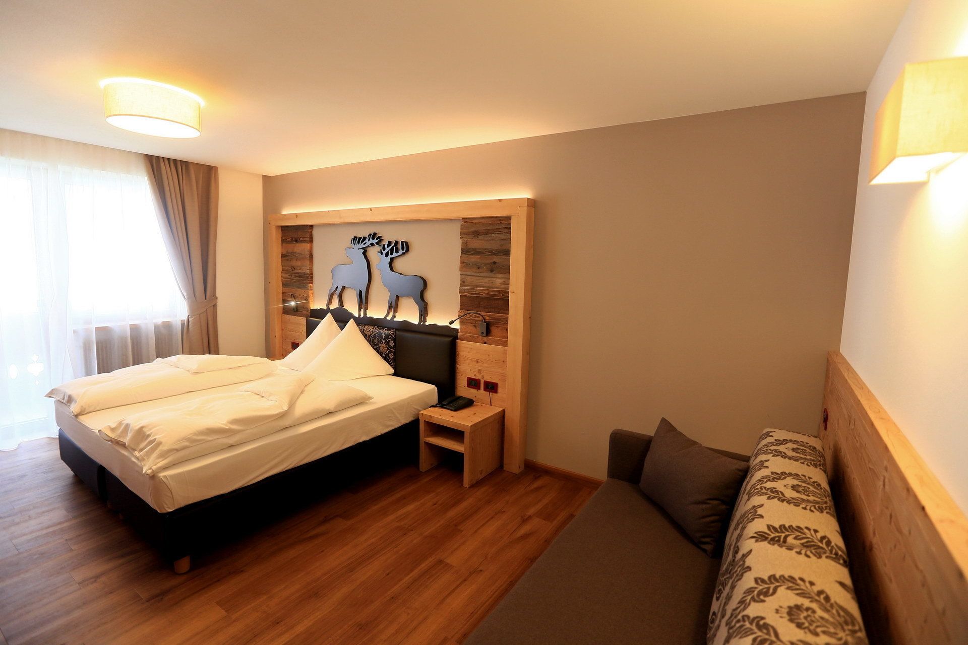 A hotel room with a bed, bedside table, lamp, and a wall-mounted artwork of deer.
