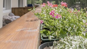 Ein Holzbalkon mit Blumentöpfen und Blumen, mit Blick auf eine Berglandschaft.