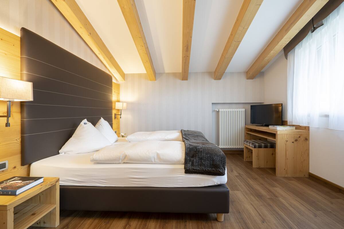 Un dormitorio moderno con una cama grande, cabecera de madera, lámparas de noche, un televisor y un escritorio de madera.