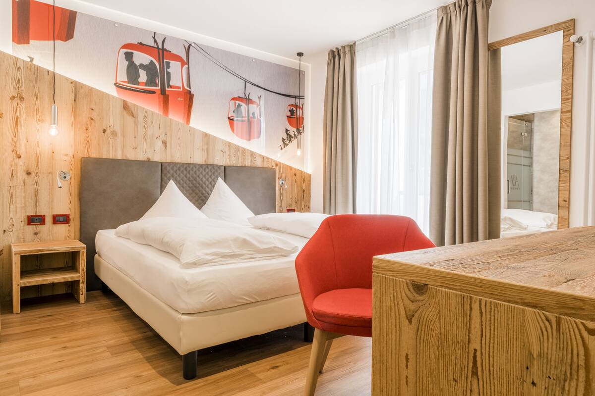 Una habitación de hotel con una cama, una silla roja, un escritorio de madera y un espejo grande.