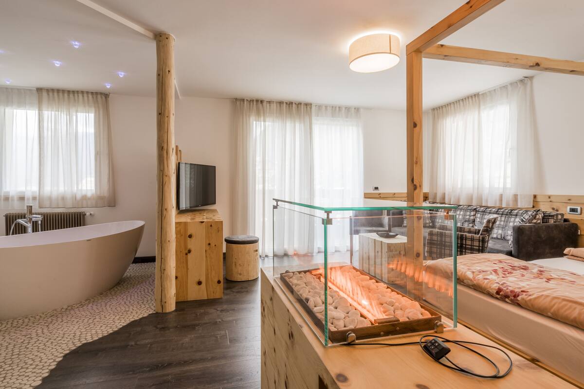 Un dormitorio moderno con chimenea de vidrio, un espejo grande, una cama de madera y una bañera.