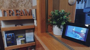 A reception desk with a wooden shelf displaying brochures and a potted plant. - Hostal Anosa Casa (Santiago de Compostela)