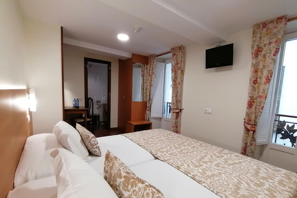A hotel room with a large bed, a desk, a chair, and a television.