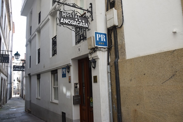 Eine schmale Straße mit einem Hostel namens 'Hostal Anosacasa' und einem Parkschild.