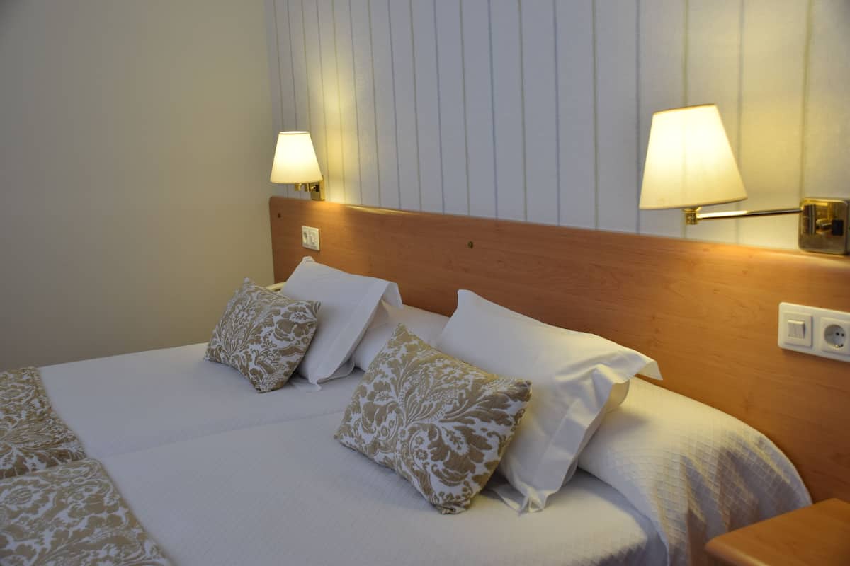 A neatly made bed with white and patterned pillows, a wooden headboard, and two wall-mounted lamps.