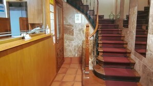 A reception area with a wooden counter, a spiral staircase with red steps, and a security camera on the ceiling. - Hostal Anosa Casa (Santiago de Compostela)