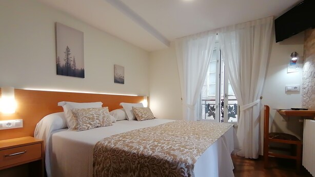 A hotel room with a bed, bedside tables, a desk, and a window with curtains. - Hostal Anosa Casa (Santiago de Compostela)