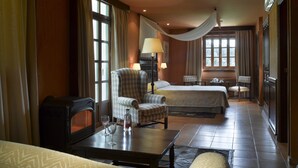 A hotel room with a bed, two armchairs, a small table with glasses and a bottle, and a radiator.