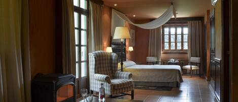 A hotel room with a bed, two armchairs, a small table with glasses and a bottle, and a radiator.