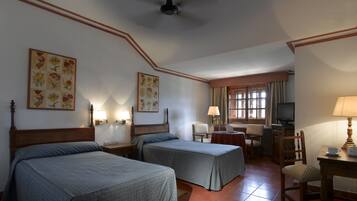 Habitación de hotel con dos camas, un escritorio, una silla, un televisor y un ventilador de techo.