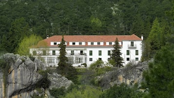A white building with a red roof, surrounded by dense green forest and rocky terrain.