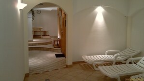 Baño con ducha, lavamanos y dos tumbonas blancas.