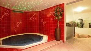 Un baño moderno con baldosas rojas, una bañera de hidromasaje, una planta en maceta y un banco.
