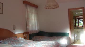 A bedroom with two beds, a wooden headboard, a hanging light fixture, a window with curtains, and a view of a bathroom.