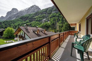A balcony with wooden railings overlooking a mountainous landscape with houses and trees.