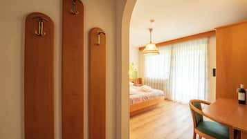 A hotel room with a wooden wardrobe, a bed with a floral bedspread, a dining table with a bottle of wine, and a chandelier.