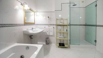 A bathroom with a bathtub, sink, mirror, glass shower enclosure, and a shelf with toiletries.