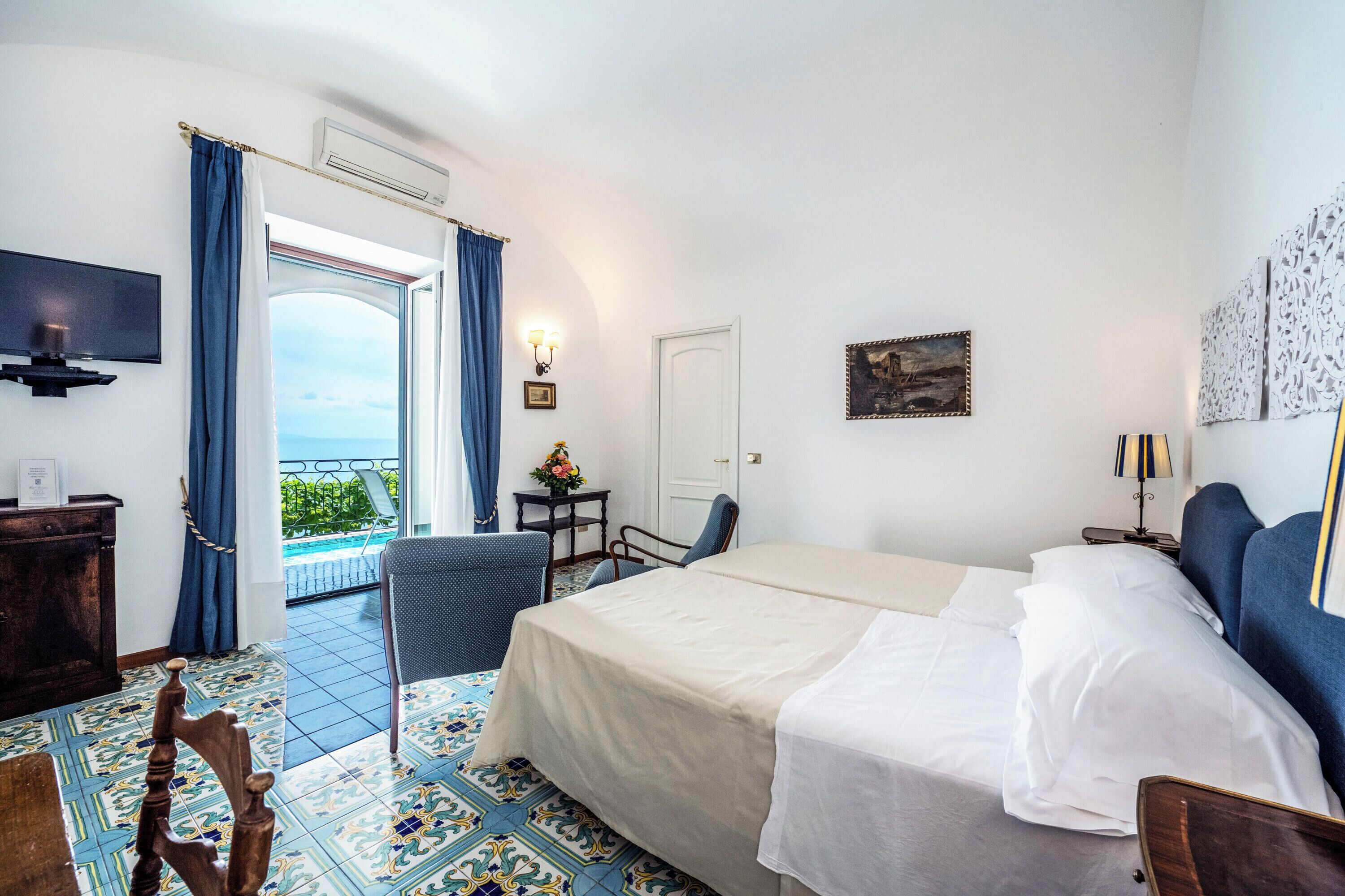 Une chambre d’hôtel avec un lit, une chaise, un bureau, une télévision et une vue sur la mer.