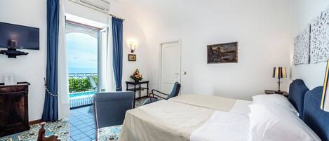 Une chambre d’hôtel avec un lit, une chaise, un bureau, une télévision et une vue sur la mer.