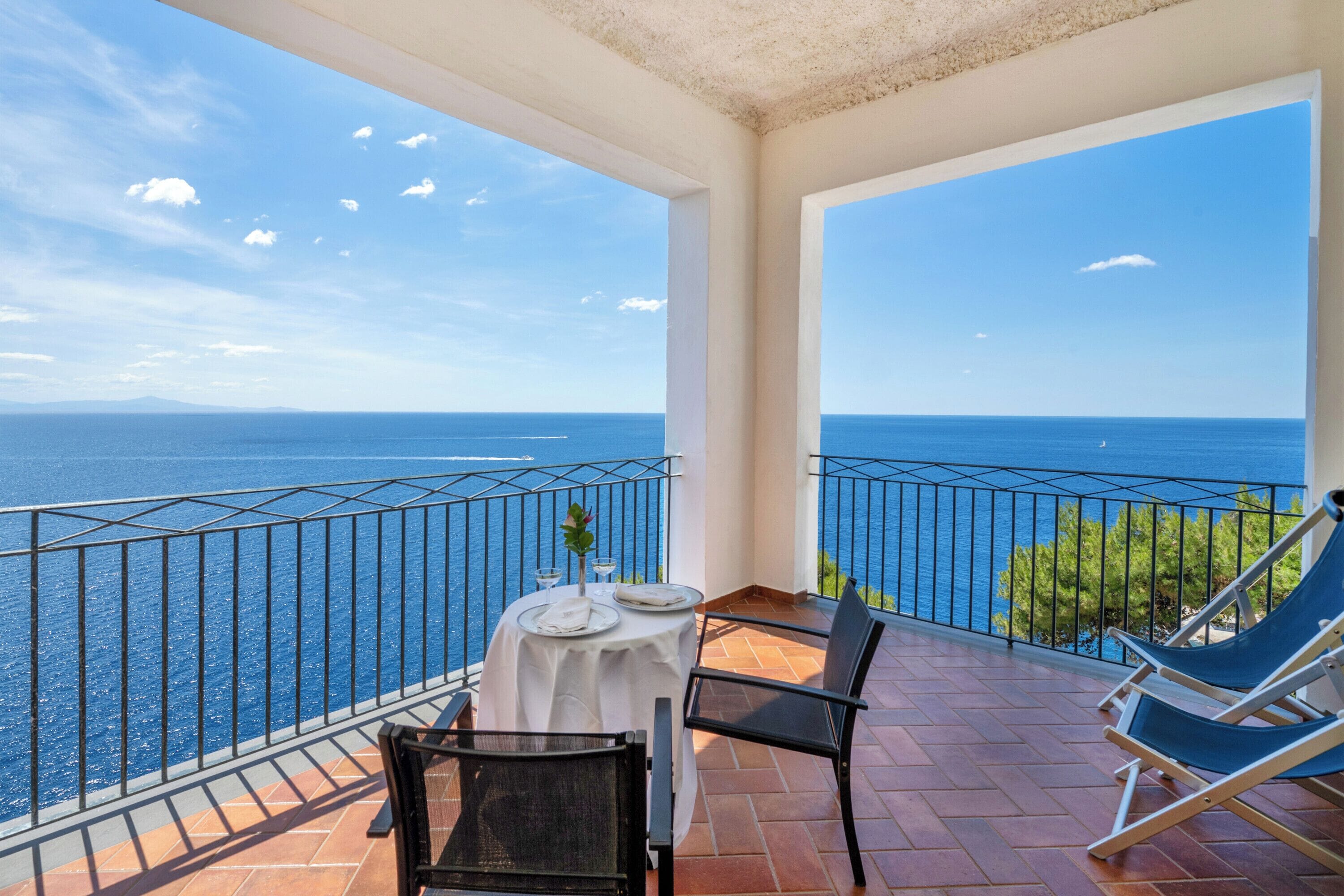 Un balcon avec une table dressée pour deux personnes, donnant sur une mer d’un bleu limpide.