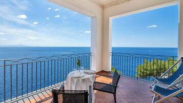 Un balcon avec une table dressée pour deux personnes, donnant sur une mer d’un bleu limpide.
