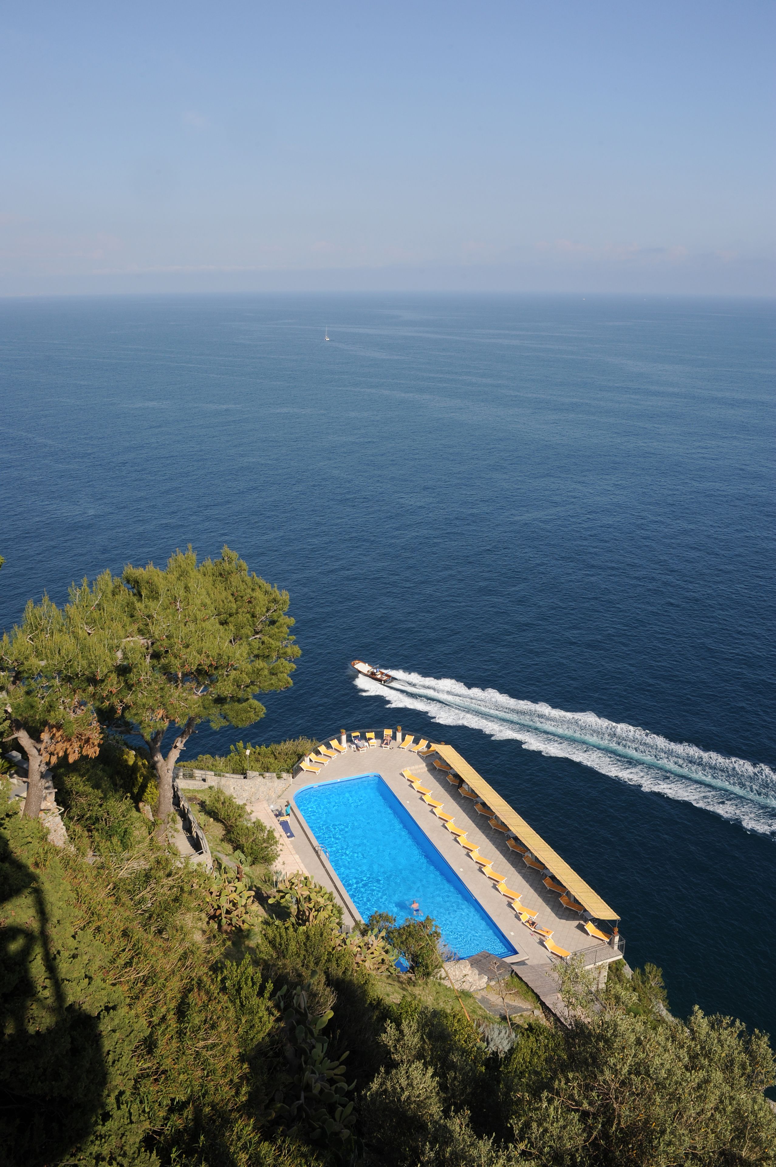 A pool with a view of the sea, surrounded by trees.