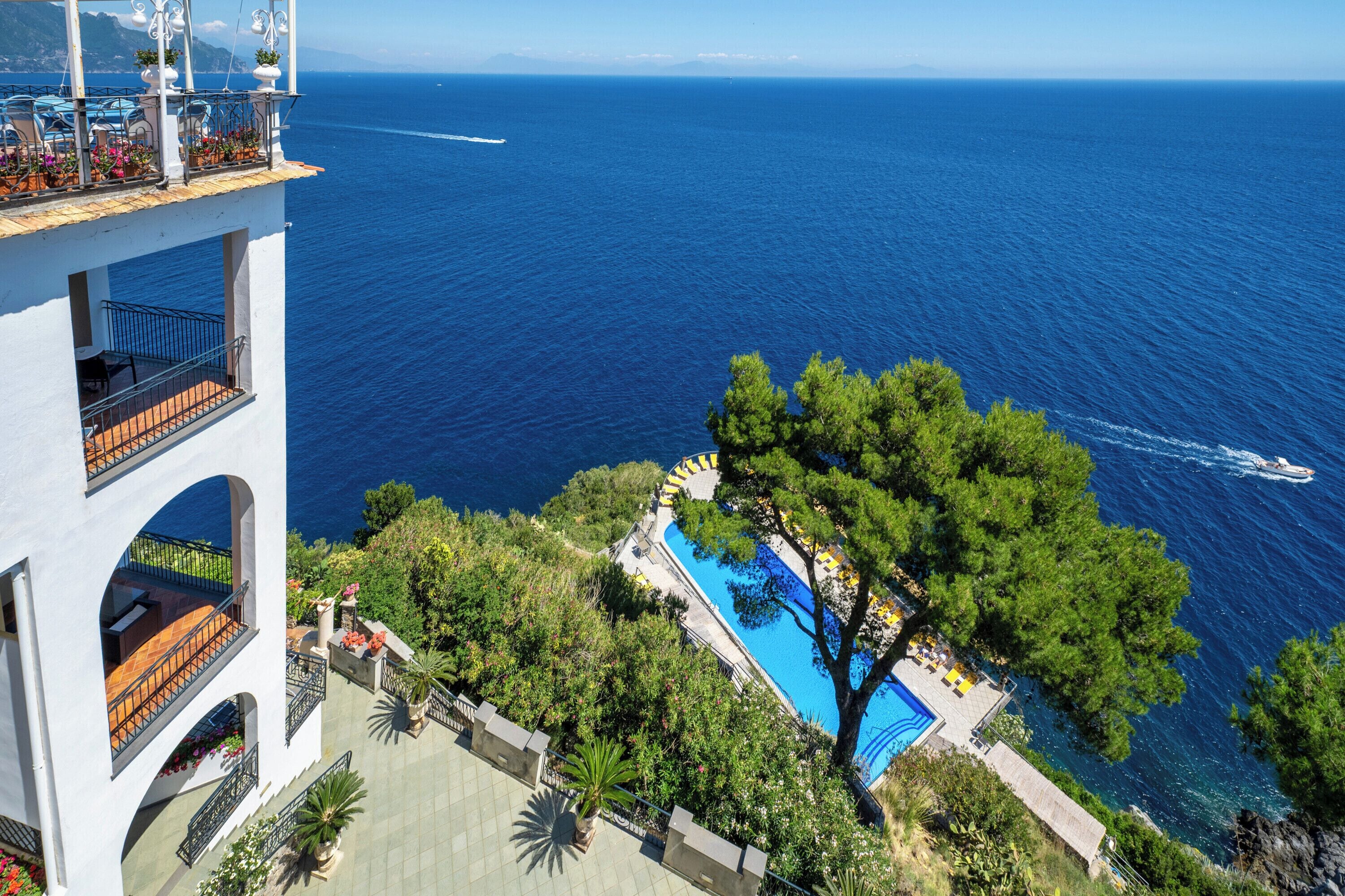 A high-rise hotel with a pool surrounded by greenery and a view of the sea.