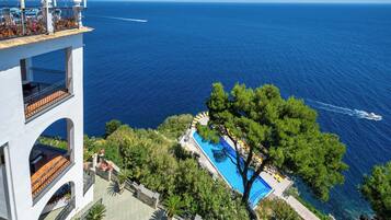 A high-rise hotel with a pool surrounded by greenery and a view of the sea.