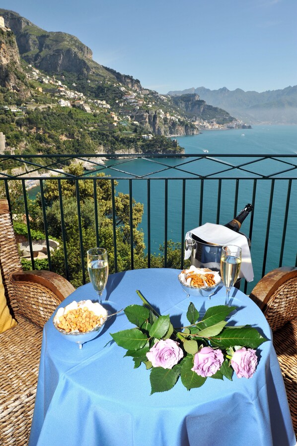 Une table dressée avec une bouteille de champagne, un verre de vin et un bol de collations, le tout placé sur un balcon donnant sur un paysage côtier.