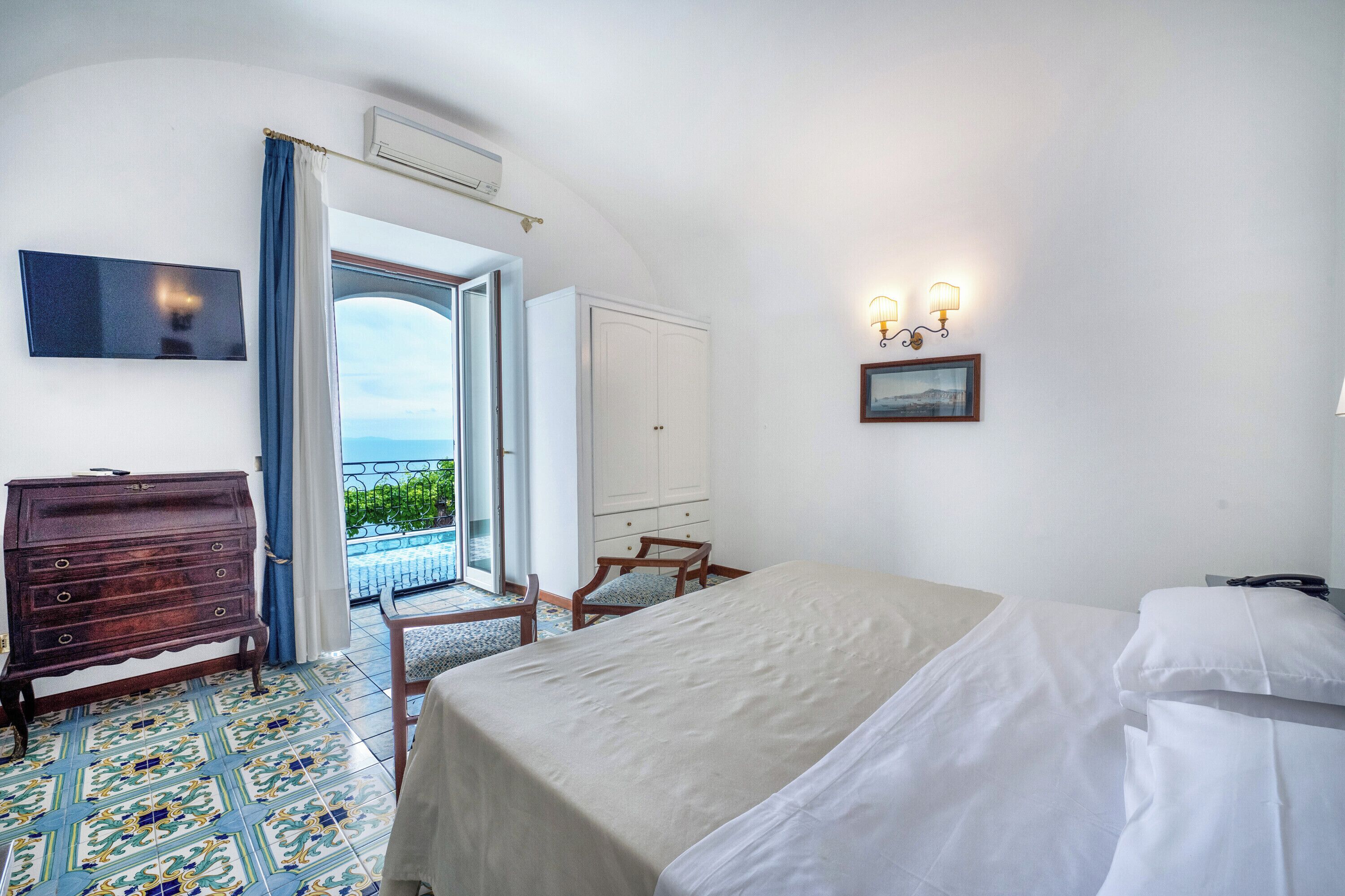 A hotel room with a bed, a dresser, a chair, a TV, and a balcony with a view.
