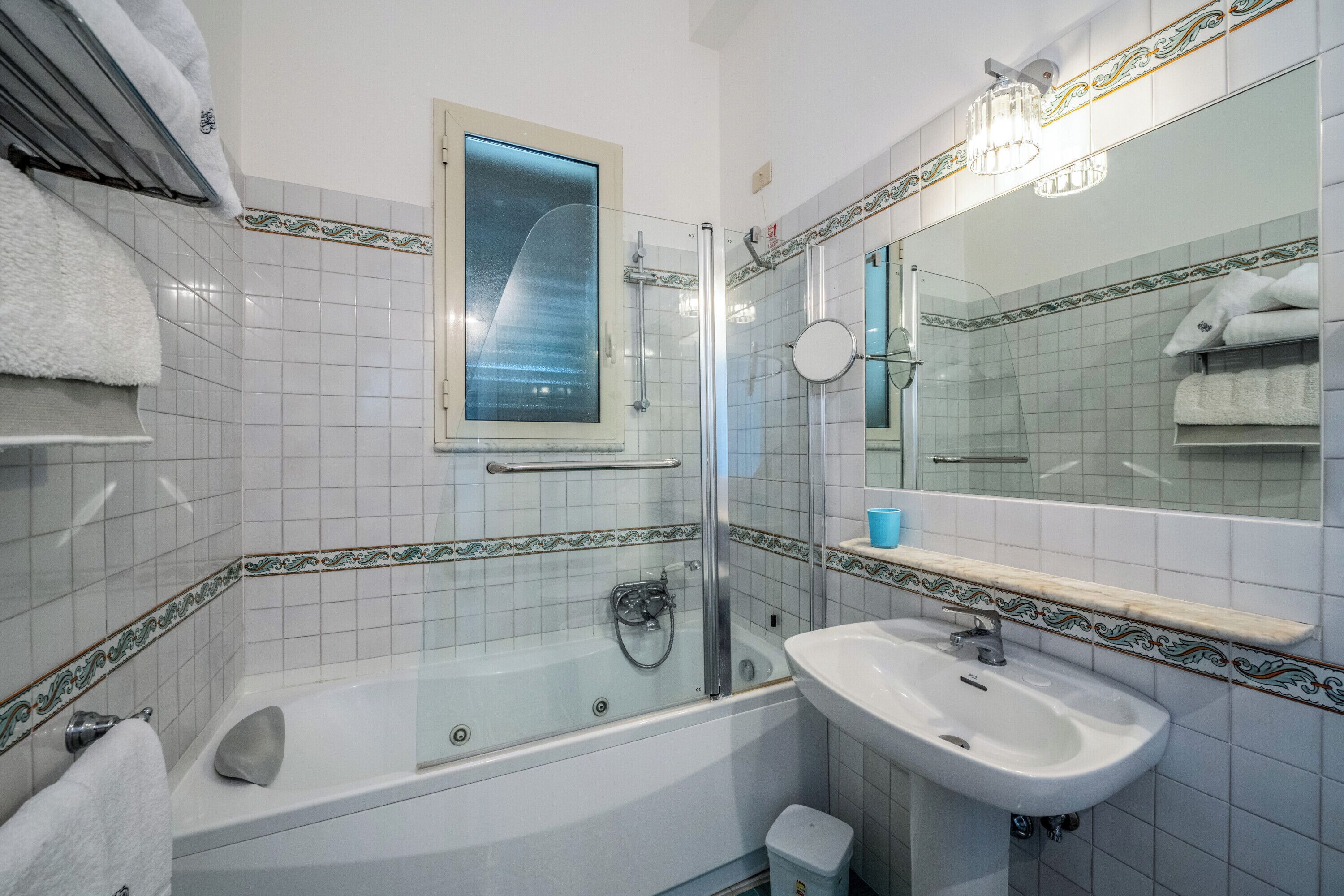 A bathroom with a bathtub, a sink, a glass shower enclosure, and a mirror with a decorative border.