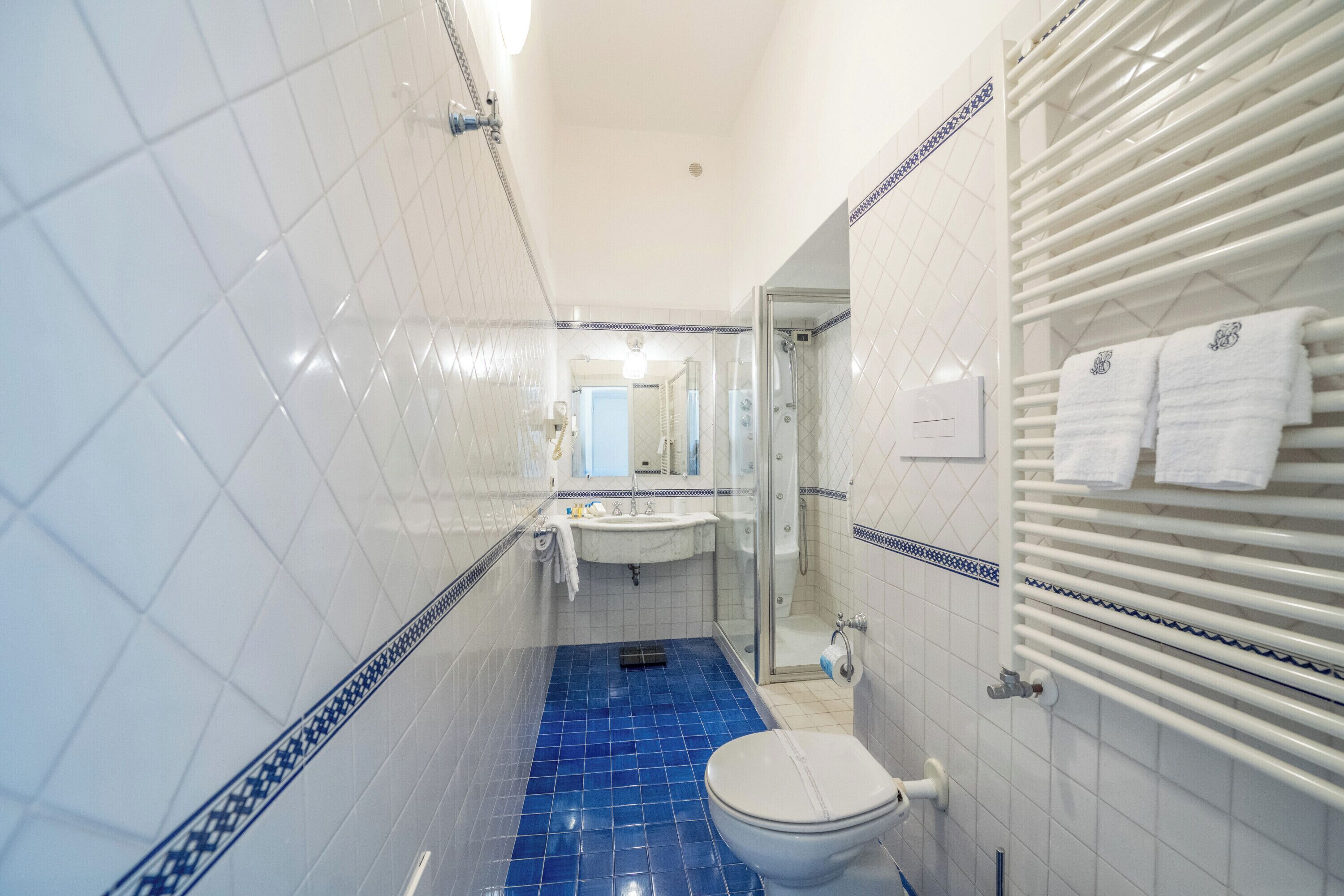 A bathroom with white tiled walls, a blue-tiled floor, a white sink, a toilet, and a glass-enclosed shower.