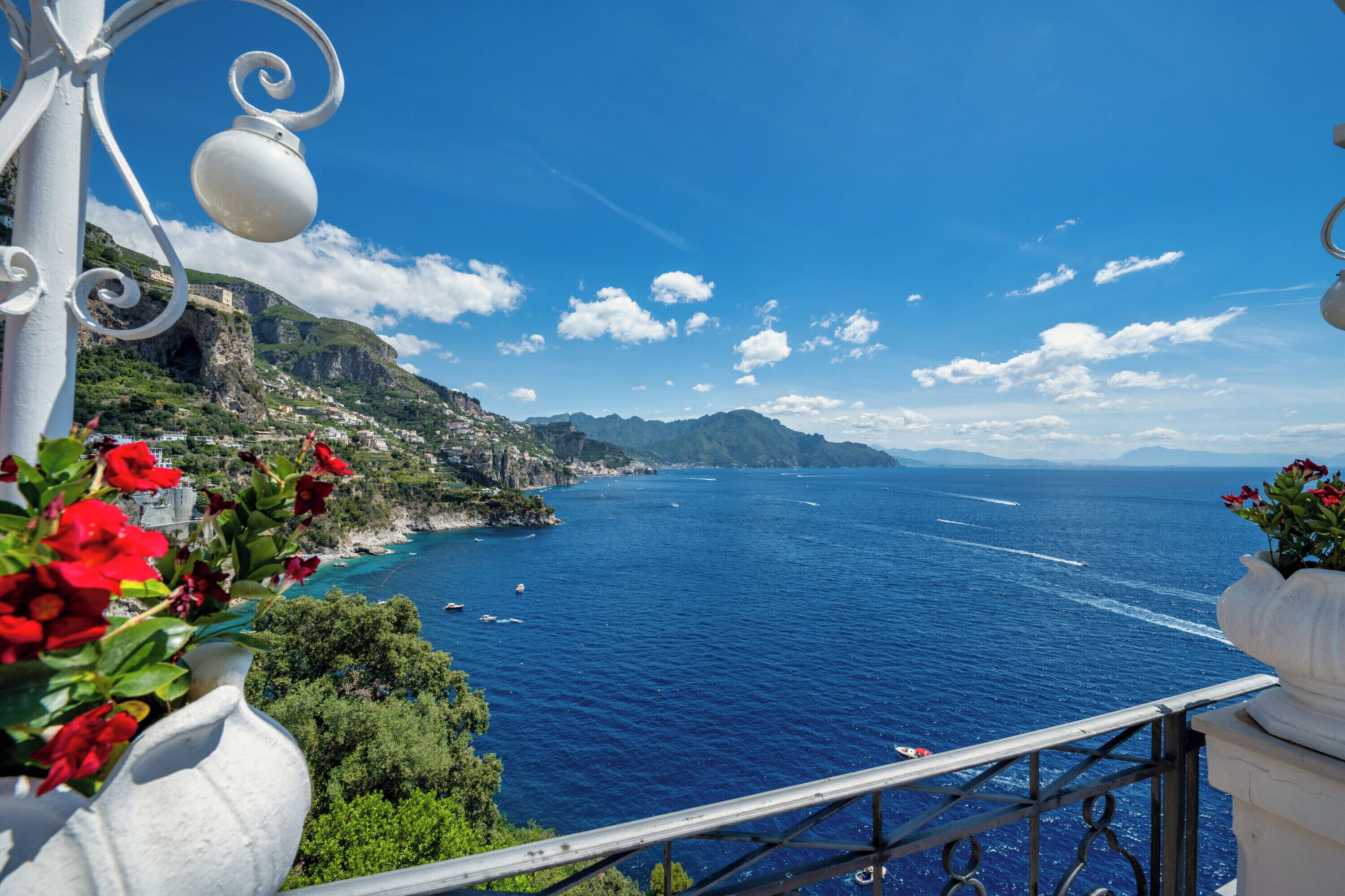 A coastal view with a balcony, a white railing, and a clear blue sea.