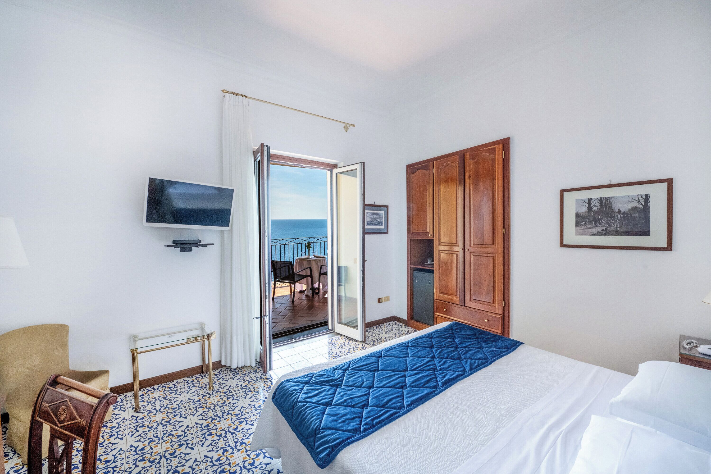 A hotel room with a bed, a television, a wooden wardrobe, a desk, and a chair.
