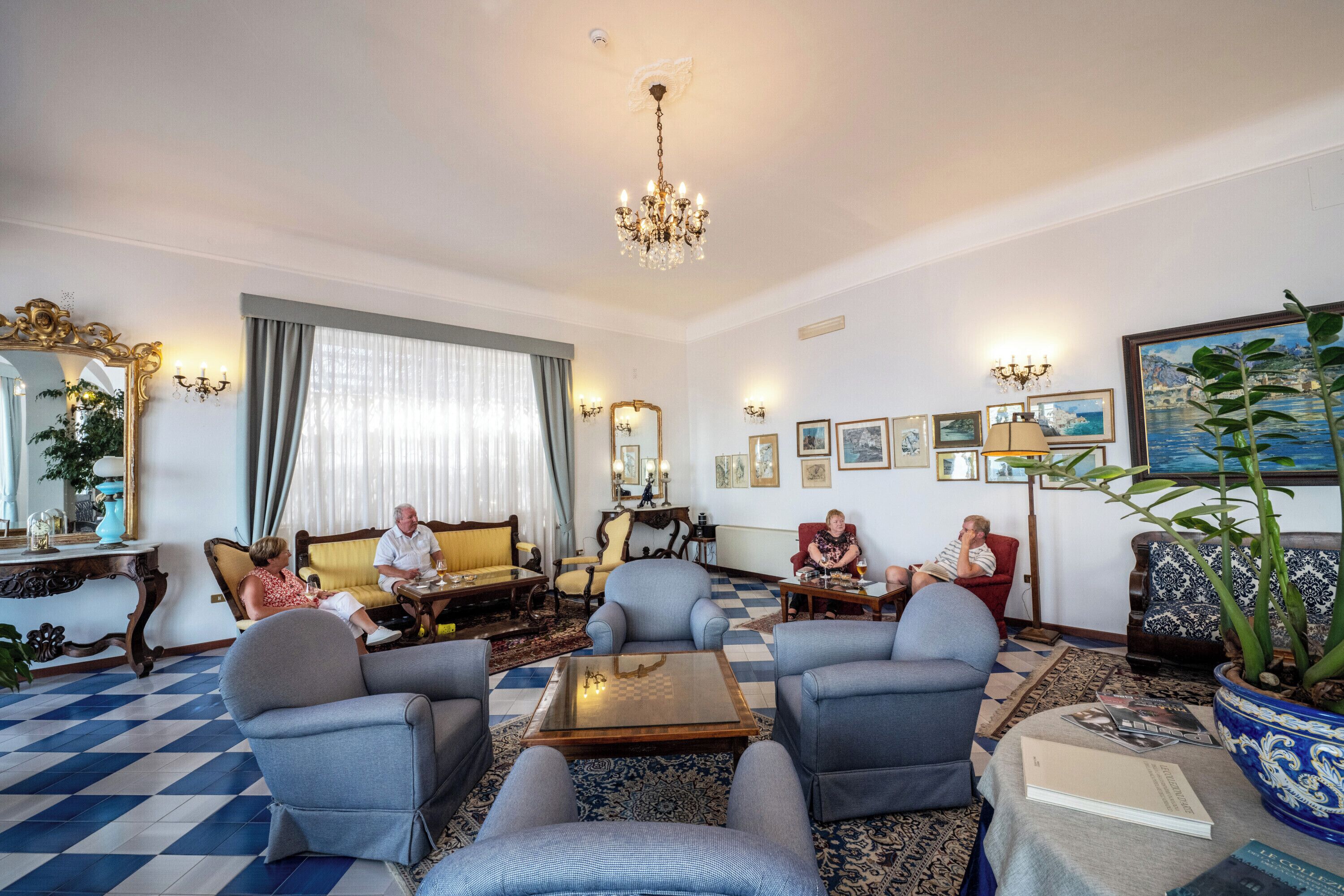 A spacious living room with a checkered floor, a chandelier, and a large potted plant.