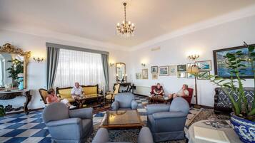 A spacious living room with a checkered floor, a chandelier, and a large potted plant.