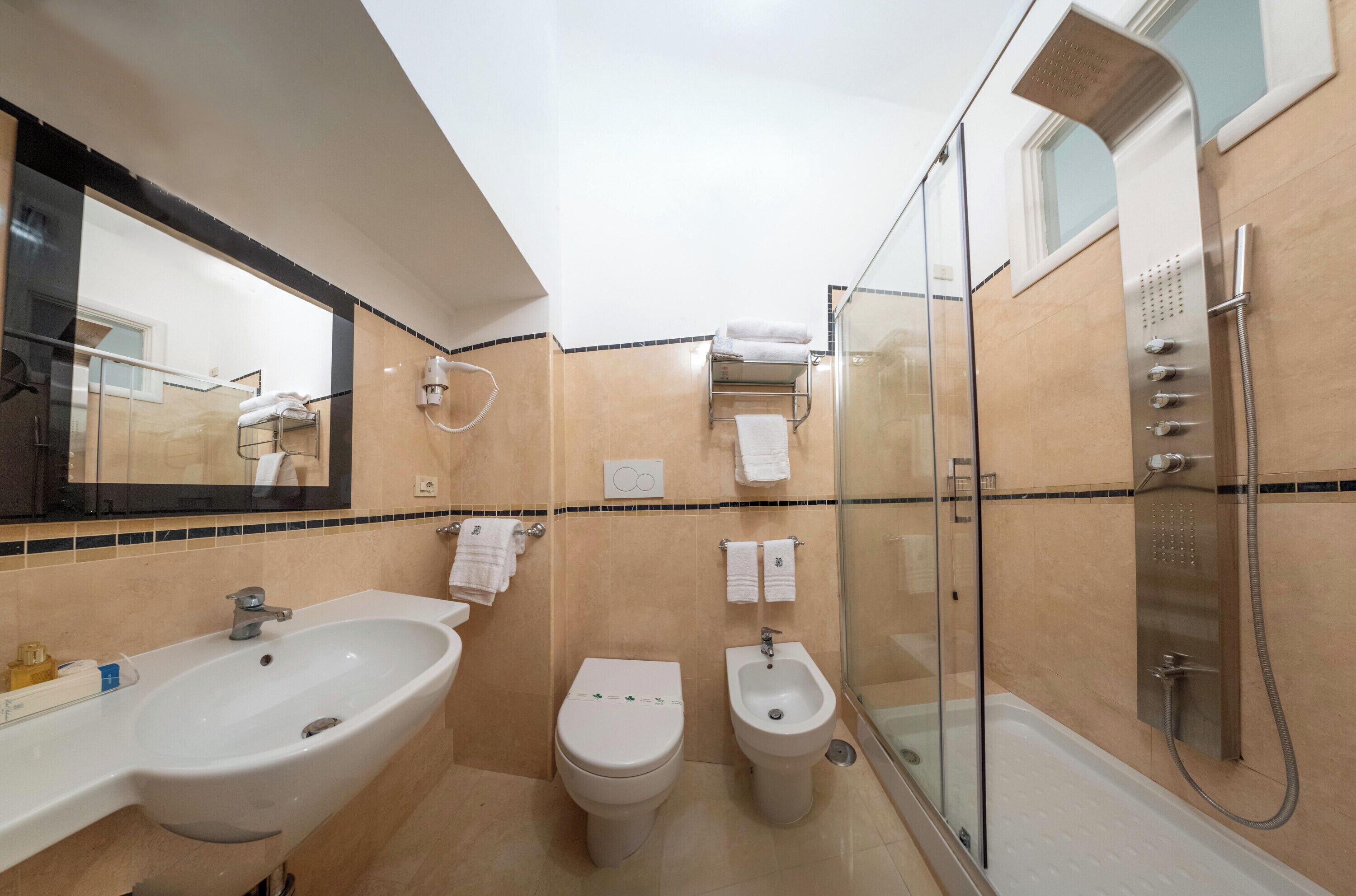 A modern bathroom with a large sink, toilet, bidet, and a glass-enclosed shower area.