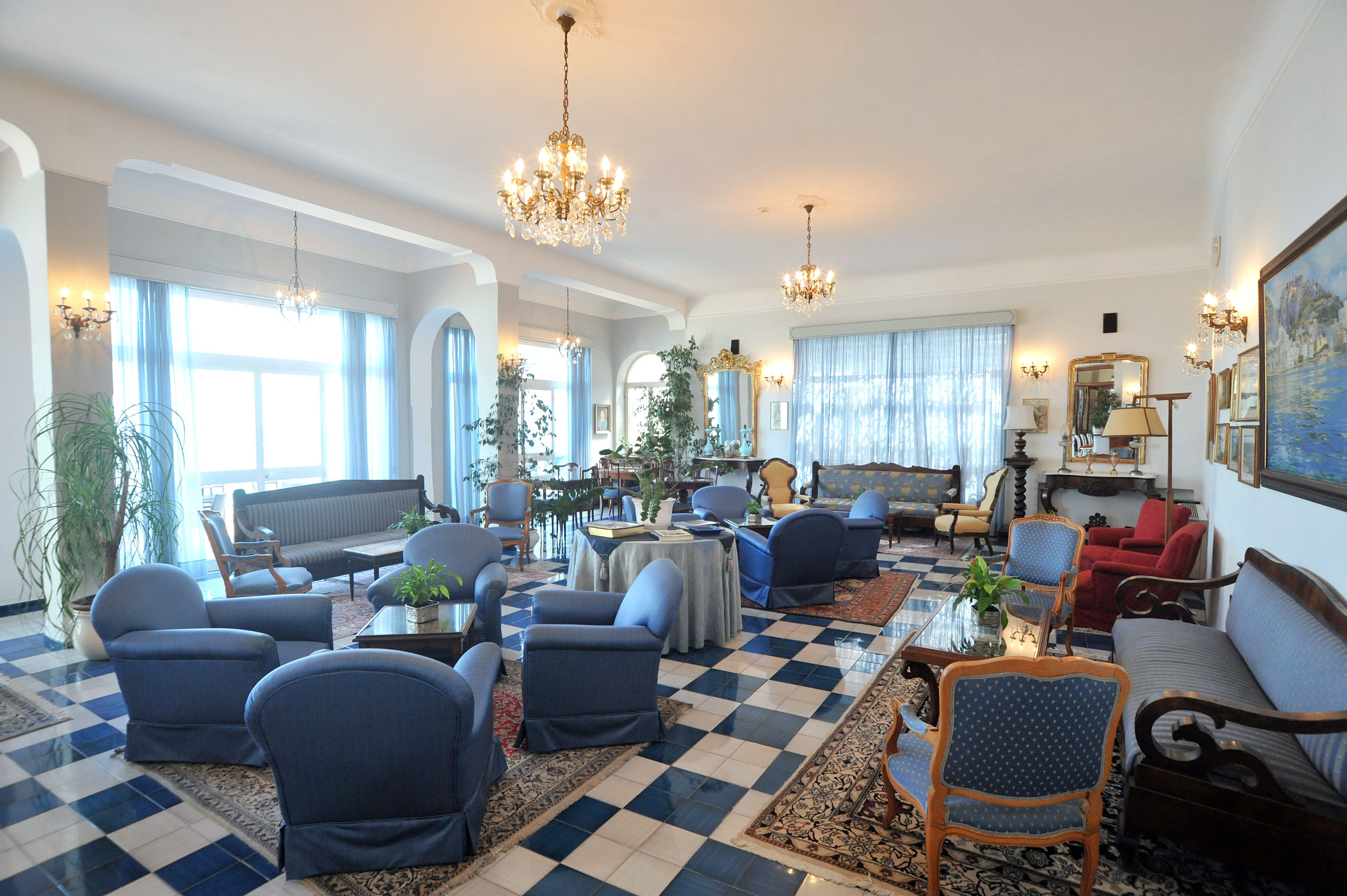 Ein geräumiges Wohnzimmer mit Schachbrettmuster-Boden, mehreren Sitzgelegenheiten und großen Fenstern, die viel Tageslicht hereinlassen.